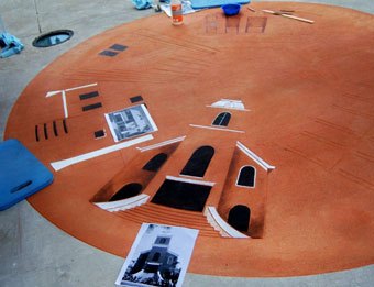 A circular design being etched into a red concrete entrance walkway, with stencils and tools still in place