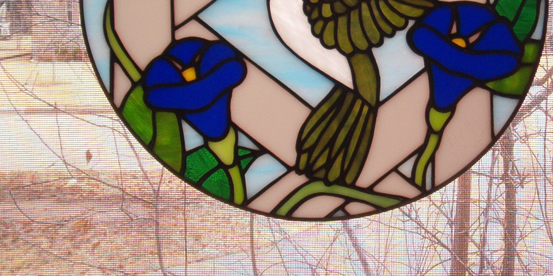 Stained glass panel of a hummingbird at blue morning glories, set in a window.