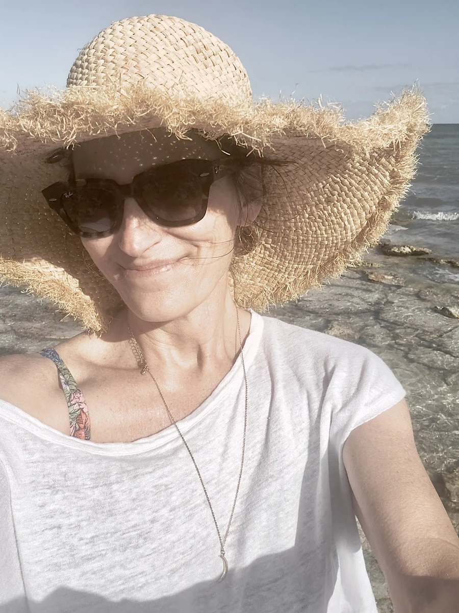 Dawn "Cricket" Desmarais on the shoreline in a wide straw hat and sunglasses