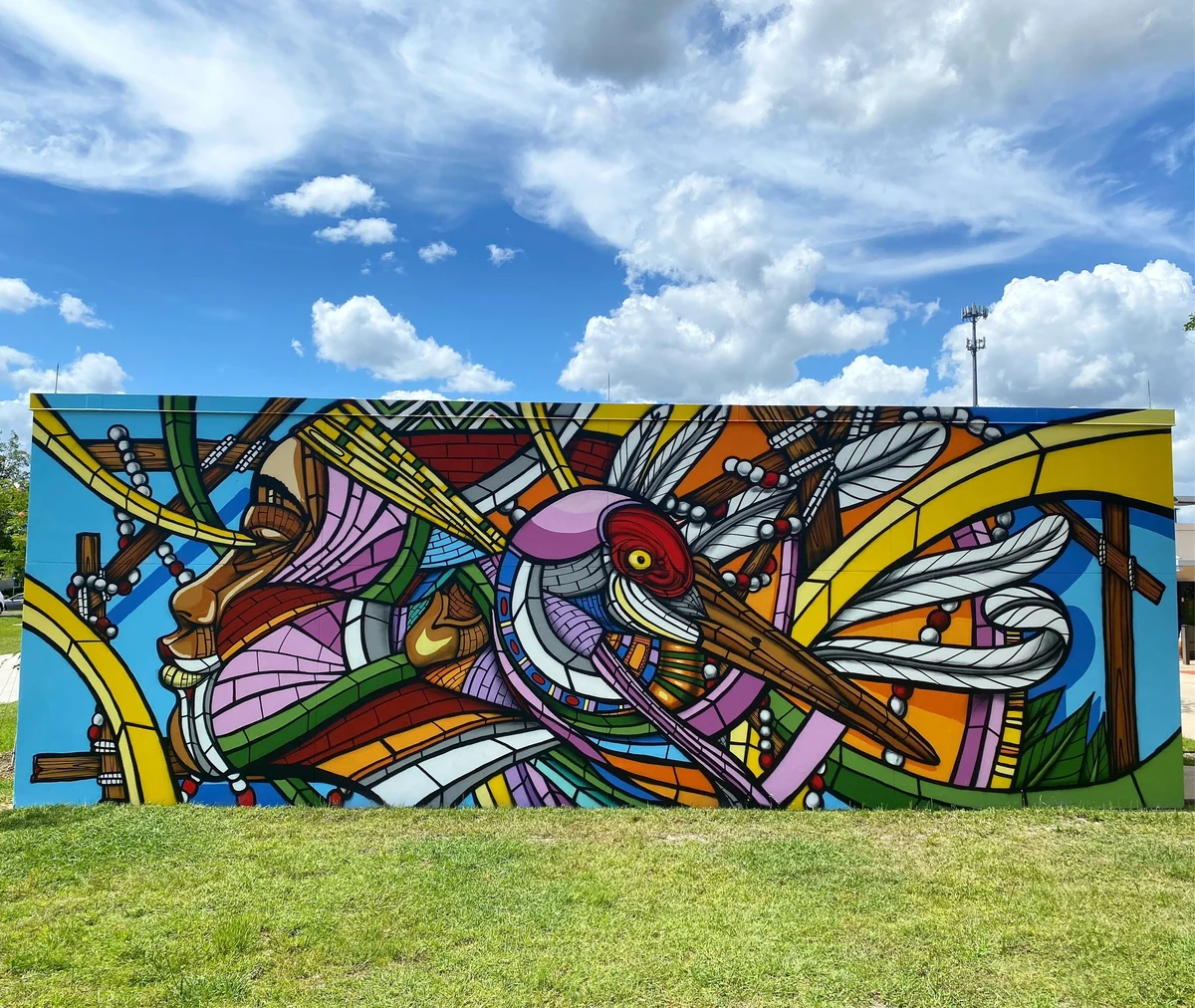 Valencia, freestanding outdoor mural of a face in profile merged with a large bird and feathered wings, in pink, yellow and blue
