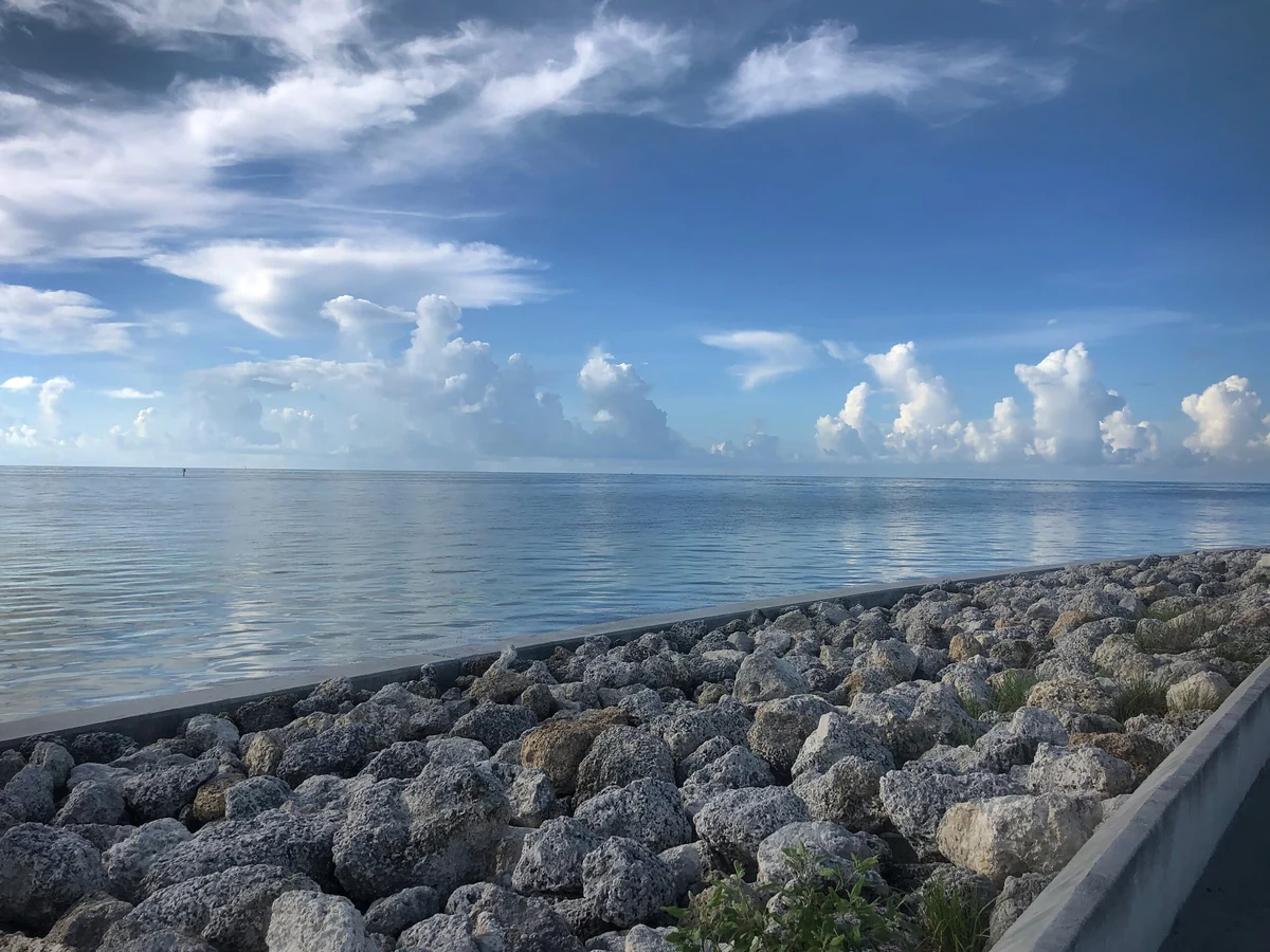 Day 111, from the 398 Days photographic series: a rock revetment along the water under a wide Keys sky of cumulus cloud