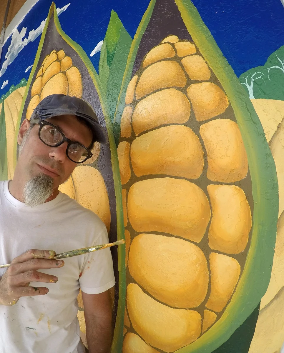 Gerry Stecca, brush in hand, beside the corn mural he painted for the Regency Centers commission