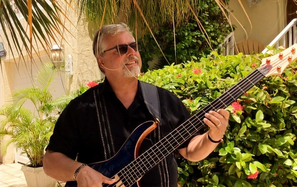 Jeff Dalton playing a five-string electric bass outdoors in a garden