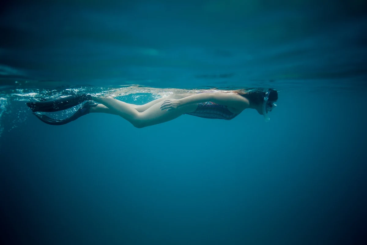 A free diver in mask and fins gliding just under the surface in clear teal water