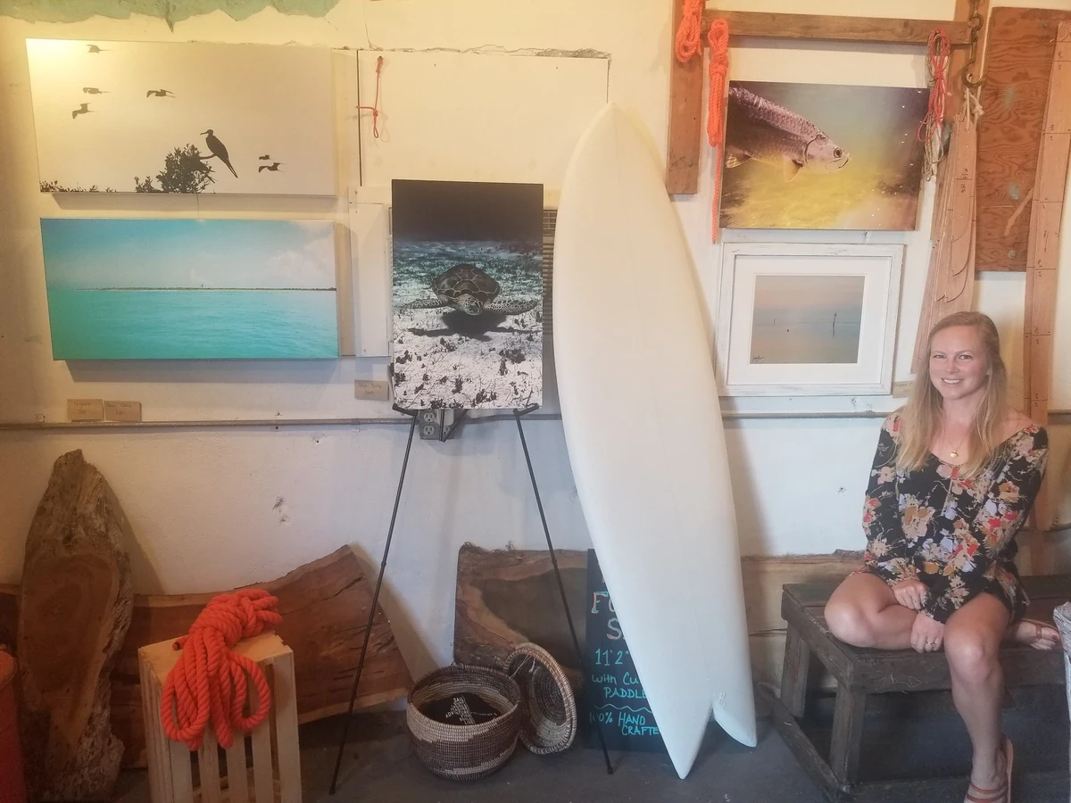 Jessica Connell seated beside her framed prints of shorebirds, sea turtles and Keys water at a show booth