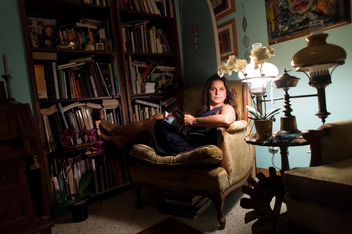 Natalie Plasencia at home, seated in an armchair beside her bookshelves