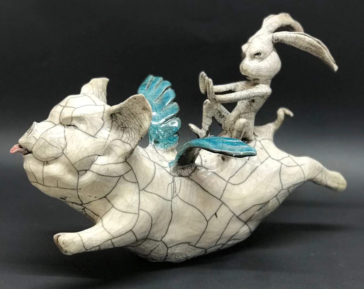 Raku-fired ceramic sculpture of a winged flying pig with a rabbit riding on its back, crackle-glazed white with turquoise wings